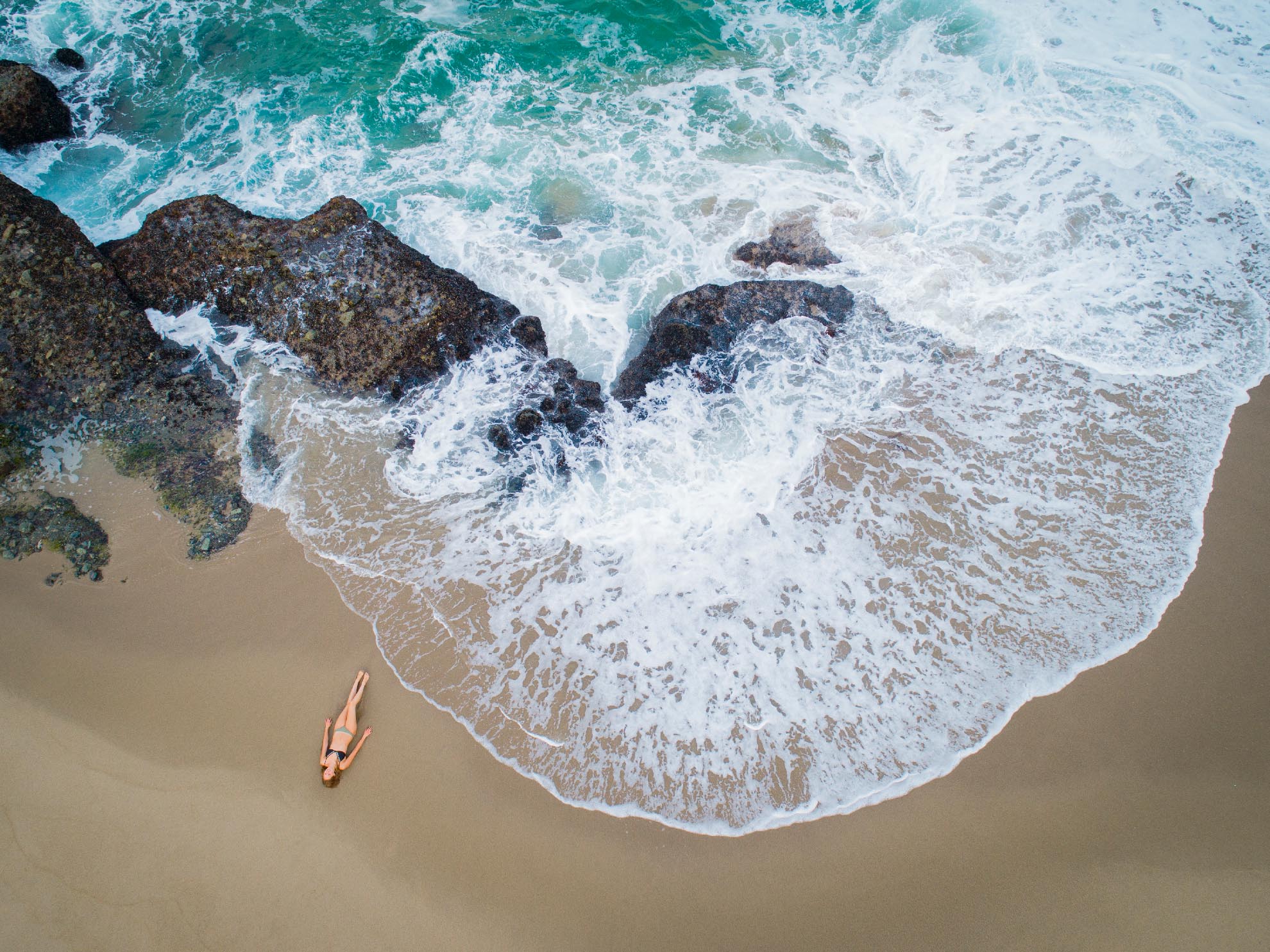 Drone Photograph of birds eye view of woman lying on Table Rock beach California in a bikini