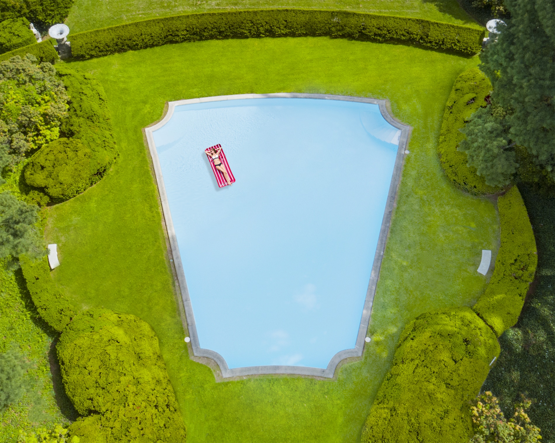 Drone Photograph of woman in a bikini lying on a float in a vintage swimming pool