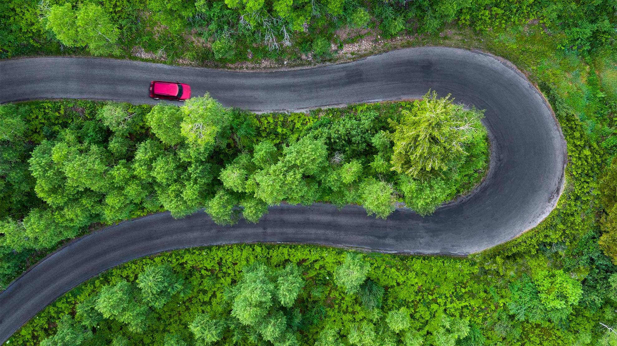 Drone photograph of birds eye view of red vehicle traveling on a horse shoe road