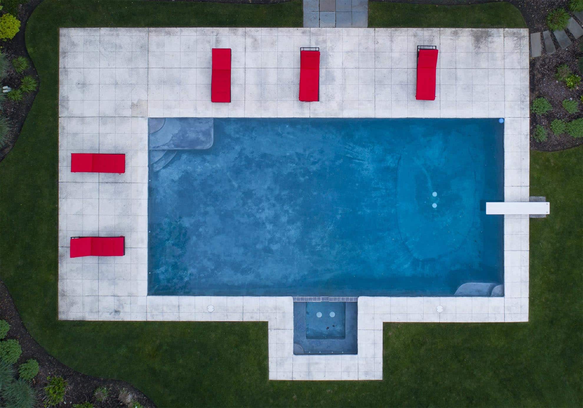 Drone photograph of birds eye view of Blue swimming pool with red chairs